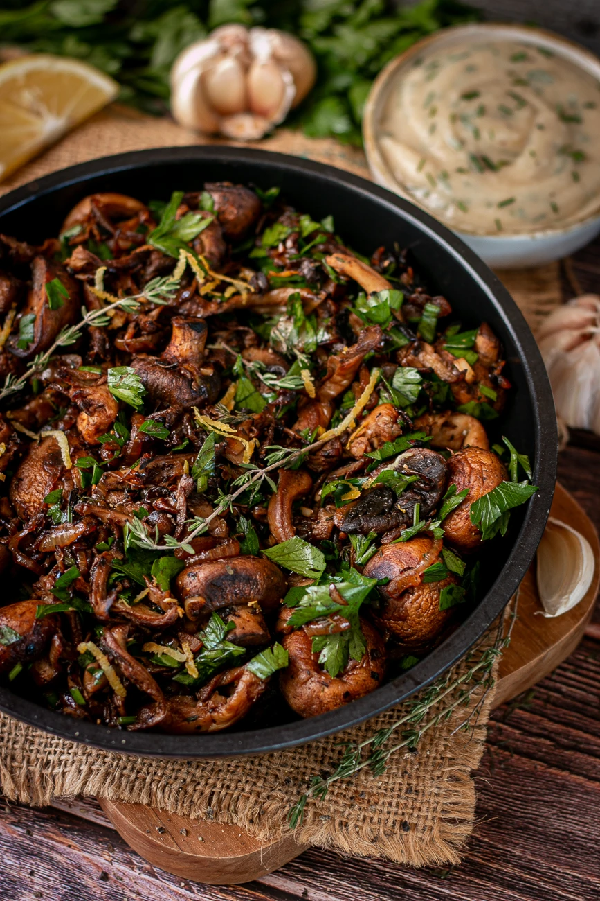 Vegane Pilzpfanne mit gebratenen Champignons und Austernpilzen, Petersilie und Zitronenabrieb, daneben eine Schale Knoblauchdip