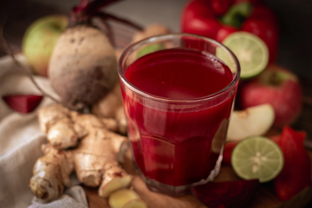 Ein Glas Rote Bete Saft und Zutaten wie Rote Bete, Äpfel, rote Paprika, Limette und Ingwer 
