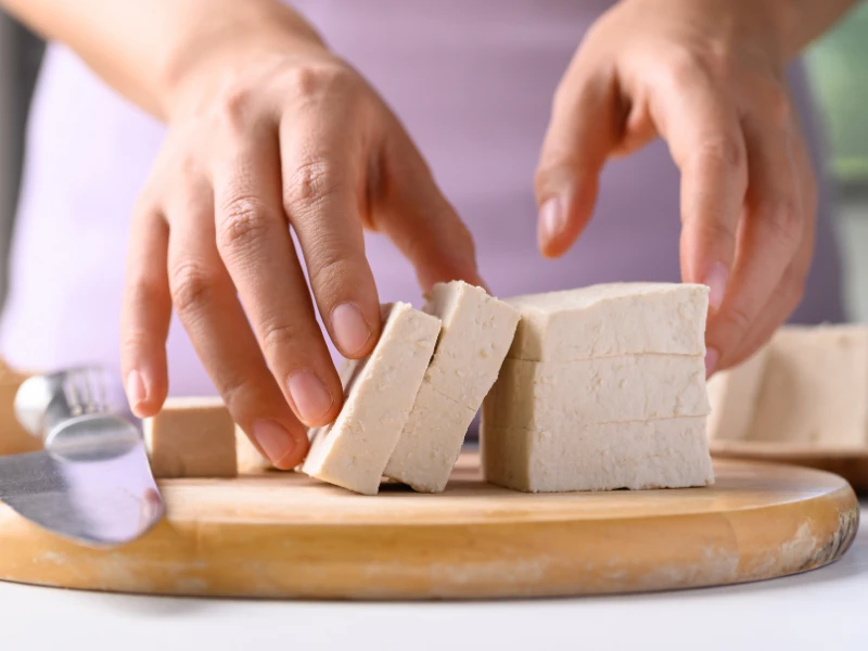 Hände schneiden Tofu auf einem Holzbrett, Soja als Teil einer veganen Ernährung in den Wechseljahren